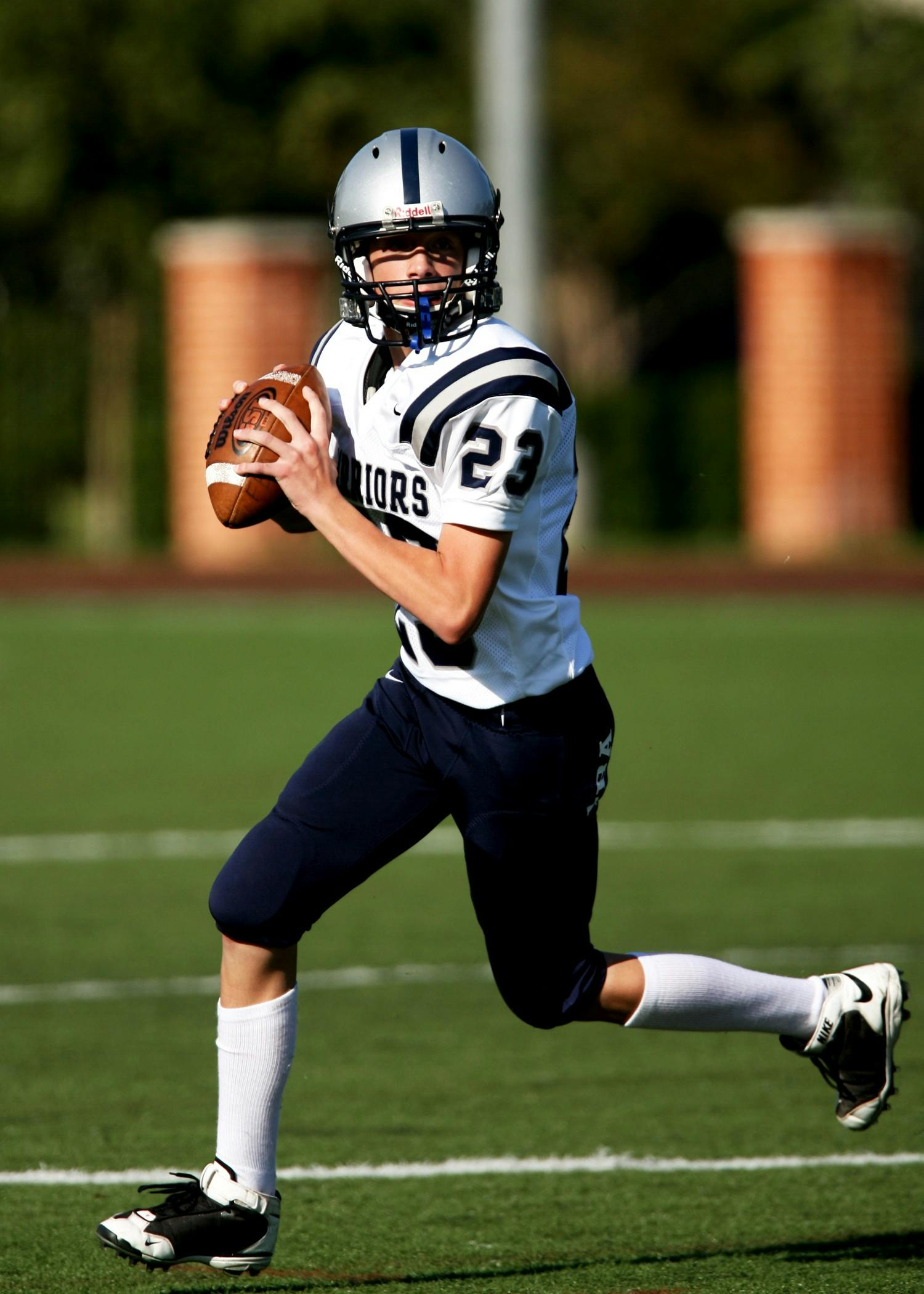 Young quarterback running with a football during a game on a sunny day.